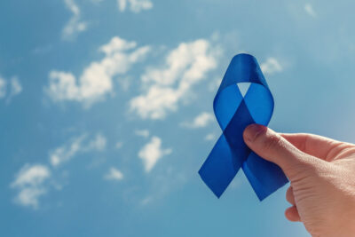 Hand holding blue ribbon on blue sky background , Prostate Cancer Awareness, Men health awareness, November blue, International Men's Day, world diabetes day